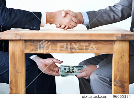 Under-the-table transactions.... Cropped shot of two businessmen shaking hands while money passes hands under a table. Under-the-table transactions.... Cropped shot of two businessmen shaking hands while money passes hands under a table. 96065354