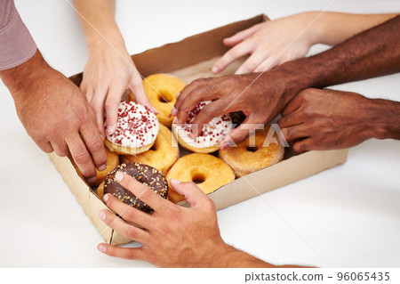 Take a bite of inspiration. A multitude of hands reaching to grab a doughnut from a box. 96065435