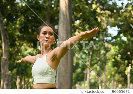 Sporty millennial woman practicing yoga lesson, standing in Warrior II yoga pose in the park. Yoga, meditation and healthy lifestyle concept 96065671