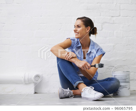White really opens the room up. Shot of a woman holding a paintbrush while sitting on a floor. 96065795