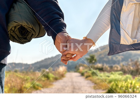 Close up of loving couple holding hands while walking on rural road in autumn or spring nature. Friendship and relationship concept. Well Being and unity with nature. Road to mountain. 96066324