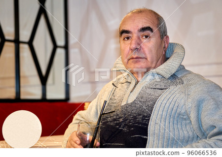 Elderly male pensioner sitting with a glass at a table in a cafe 96066536