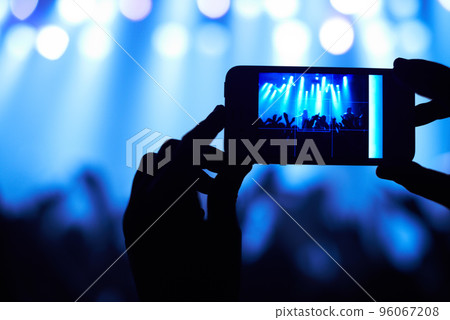 Cropped shot of a person filming their favorite band with a camera phone. This concert was created for the sole purpose of this photo shoot, featuring 300 models and 3 live bands. All people in this Cropped shot of a person filming their favorite band with a camera phone. This concert was created for the sole purpose of this photo shoot, featuring 300 models and 3 live bands. All people in this 96067208