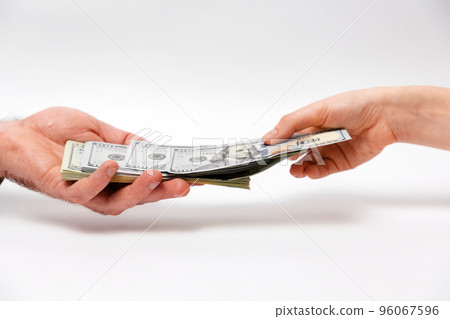 International Anti-Corruption Day. Woman pulls money out of bundle of dollars lying on man's palm. Close-up of hands on white background. Concept of bribery and investment 96067596
