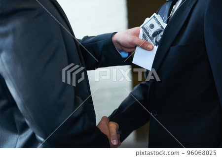 The rotten egg in the corporate world - deceptive deals. Two corporate businessmen shaking hands while one man places money in the otherampamp039s pocket. 96068025