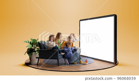 Cheering for favourite team. Young emotional friends watching football match, sport show or movie together. Excited girls and boys sitting in front of huge 3D model of tv screen Cheering for favourite team. Young emotional friends watching football match, sport show or movie together. Excited girls and boys sitting in front of huge 3D model of tv screen 96068039