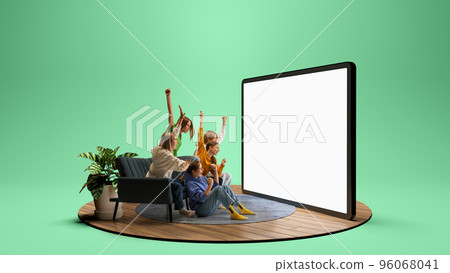 Group of young emotional friends watching football match, sport show or movie together. Excited girls and boys sitting in front of huge 3D model of device screen at home interior 96068041