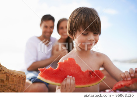 Juicy and sweet. A happy little boy biting into a watermelon with his parents looking on. 96068120