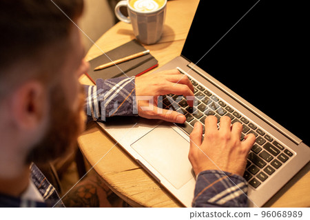 Young man drinking coffee in cafe and using laptop. Man's hands using laptop during coffee break Young man drinking coffee in cafe and using laptop. Man's hands using laptop during coffee break 96068989