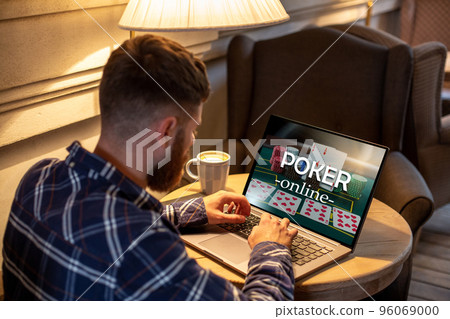 Young man playing poker via netbook during work-break in coffee shop, male sitting in front open laptop computer. 96069000