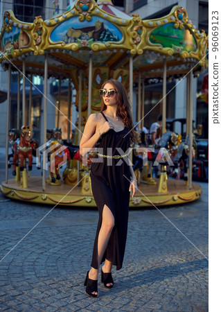 Portrait of a beautiful brunette woman in evening dress next to a children's carousel. Portrait of a beautiful brunette woman in evening dress next to a children's carousel. 96069123