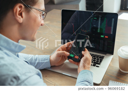 Crypto trader smiling looking at raised charts of crypto market on screens of laptop and phone 96069182