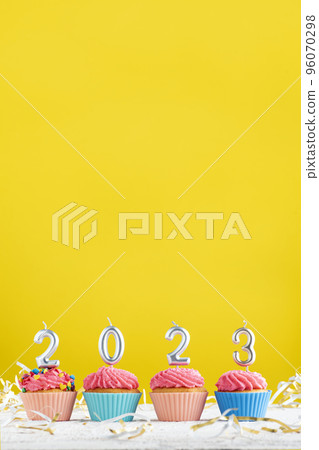 Bright Christmas theme with candles in the shape of numbers 2023 on cupcakes on yellow background. Copy space. Bright Christmas theme with candles in the shape of numbers 2023 on cupcakes on yellow background. Copy space. 96070298