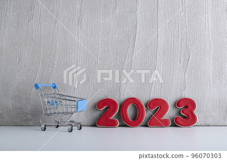 Small trolley cart and numbers 2023 on light background. Shopping for the new year. New Years discounts. 96070303
