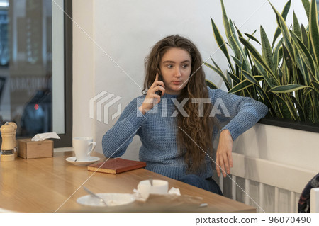 Teenager is talking on phone in cafe.Young girl with long brown hair sits in cafe with cup of tea or coffee and notebook 96070490
