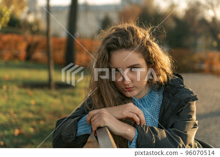 Young teenage with lush brown hair and blue eyes in autumn park looks into the camera. Girl with closer look. 96070514