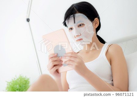 Beautiful young asian woman with sheet facial mask sitting watching tablet computer on bed. Beautiful young asian woman with sheet facial mask sitting watching tablet computer on bed. 96071121