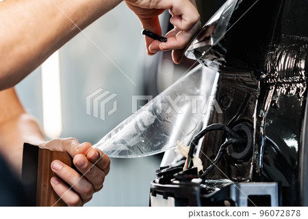 Close up of car wrapping specialist putting protective film on a car in detailing service Close up of car wrapping specialist putting protective film on a car in detailing service 96072878