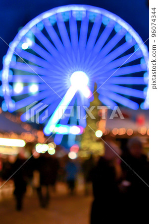 Ferris wheel decorated blue illumination, Christmas tree, black silhouettes of people walking, city buildings at winter night. Christmas Town. Beautiful New Year Christmas holiday blurred background 96074344