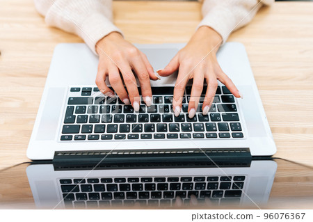 Close-up high-angle view cropped shot of unrecognizable young woman working on laptop sitting at light table in office. Female freelancer connecting to internet via computer from remote workplace. 96076367