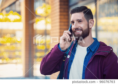Young man wearing winter clothes with a smartphone in his hand, walking in the street. Sun flare 96076763