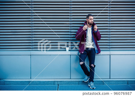 Handsome young man in purple winter jacket drinking coffee. The guy drinking coffee on the street. 96076987