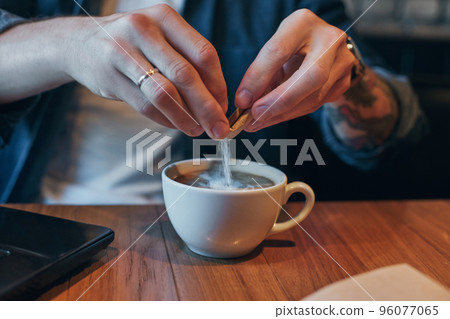 Young man drinking coffee in city cafe during lunch time and working on laptop. Close up 96077065