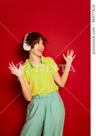 Portrait of cheerful teen girl with curly brown short hair posing in headphones isolated over red background 96077626