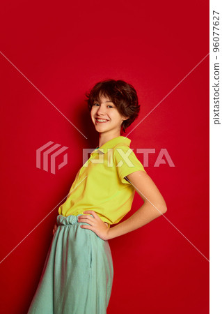 Portrait of cheerful teen girl with curly brown short hair posing on casual clothes isolated over red background 96077627