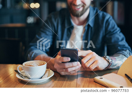 Man hands in denim shirt slide with finger on screen his smart phone, near cup with coffee on wooden table 96077783