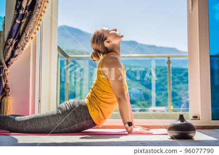 Mindful healthy woman practicing yoga at home. Sitting on the floor doing yoga for mental balance relaxing on stress. Enjoying time uses an aroma diffuser Mindful healthy woman practicing yoga at home. Sitting on the floor doing yoga for mental balance relaxing on stress. Enjoying time uses an aroma diffuser 96077790