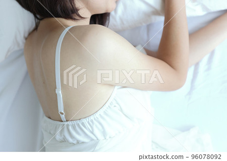 Beautiful young woman with white dress sitting in the morning at white bedroom 96078092