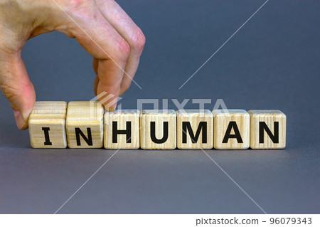 Human or inhuman symbol. Businessman turns wooden cubes and changes the word inhuman to human. Beautiful grey table grey background, copy space. Business, human or inhuman concept. 96079343
