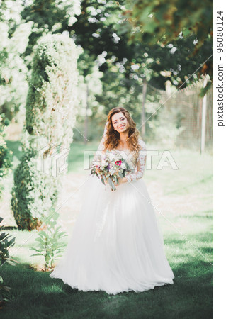 Beautiful bride posing in wedding dress outdoors 96080124