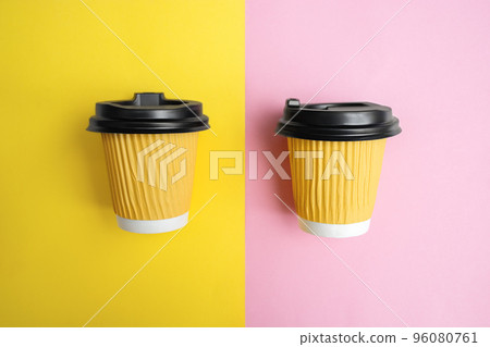 Two yellow cups for takeaway coffee or tea lie parallel on colored paper on a design table. Orange and pink background. Copy space for text. Soft Selective focus 96080761