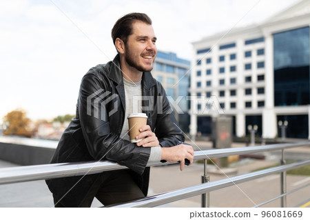 a young man with a cup of coffee in his hands stands outside and looks at the city 96081669