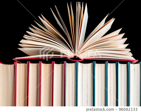 Close-up of an open book on a row of hardback books against a dark background. 96082133