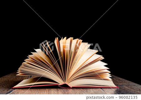 An open book with a hardcover on a wooden surface against a dark background. An open book with a hardcover on a wooden surface against a dark background. 96082135