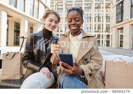 Two Smiling Young Women Using Smartphone Outside Shopping Mall Two Smiling Young Women Using Smartphone Outside Shopping Mall 96084274