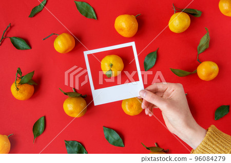 Hand holds white frames with tangerines and green leaves pattern. Xmas creative concept. Flat lay. Christmas layout. Abstract holiday textured backdrop. Creative greeting card design idea 96084279