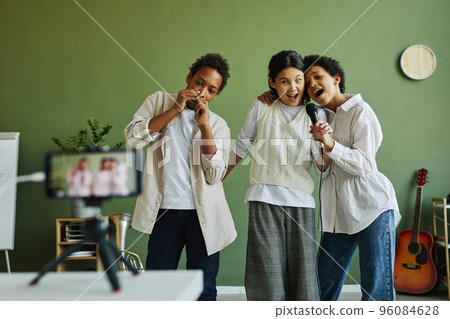 Two intercultural girls singing in microphone while boy playing harmonica Two intercultural girls singing in microphone while boy playing harmonica 96084628
