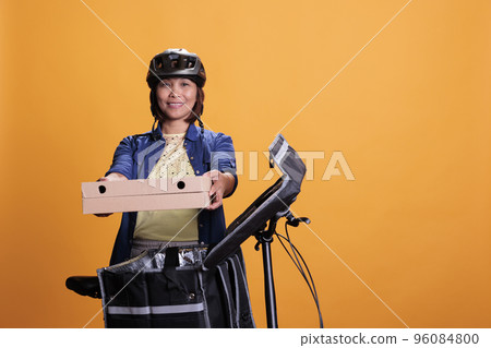 Senior take away delivery employee delivering takeout food in cardboard box to client, using bike as work transportation. Restaurant worker wearing blue t shirt and cap while working as courier Senior take away delivery employee delivering takeout food in cardboard box to client, using bike as work transportation. Restaurant worker wearing blue t shirt and cap while working as courier 96084800