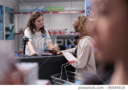 Drugstore customer paying medication treatment using terminal for contactless payment with phone during medical consultation in pharmacy. Woman buying healthcare supplements, vitamin Drugstore customer paying medication treatment using terminal for contactless payment with phone during medical consultation in pharmacy. Woman buying healthcare supplements, vitamin 96084816