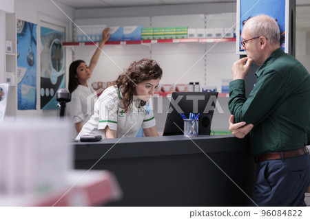 Elderly man asking drugstore worker for pharmaceutics pills during medical consultation. Helpful pharmacist checking medication list on computer, selling healthcare supplements, vitamin 96084822