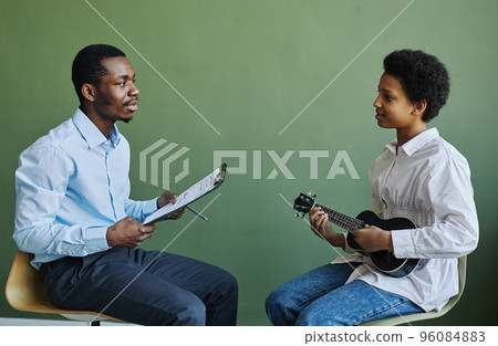 Happy youthful schoolgirl with ukulele consulting with her teacher at lesson 96084883