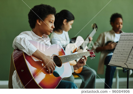 African American schoolgirl with acoustic guitar looking at paper with notes 96084906