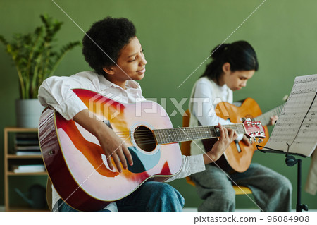 Schoolgirl with acoustic guitar looking at paper with notes on music stand 96084908