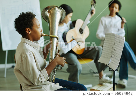 Side view of pre-teen schoolboy blowing wind instrument against classmates Side view of pre-teen schoolboy blowing wind instrument against classmates 96084942