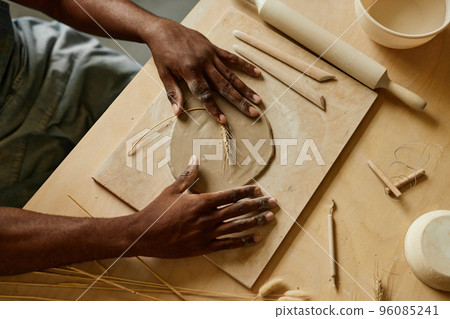 Artisan decorating handmade ceramics with plant imprint using wheat 96085241