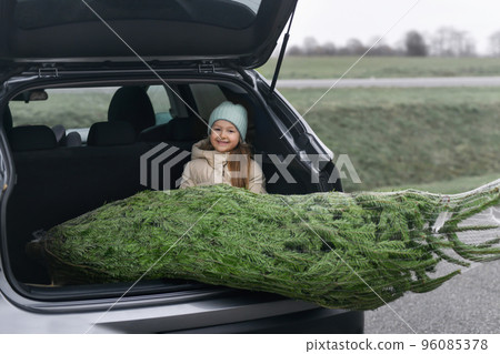 Girl sitting in the trunk with a Christmas tree Girl sitting in the trunk with a Christmas tree 96085378